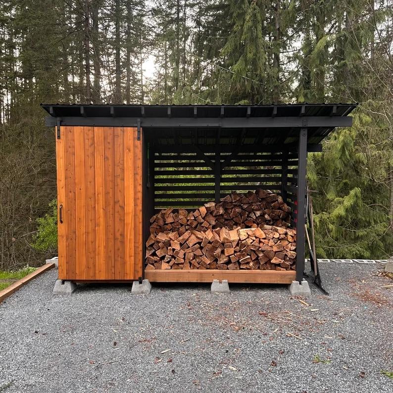 A custom built wood storage shed with logs in it, a sliding door, and tool storage. 