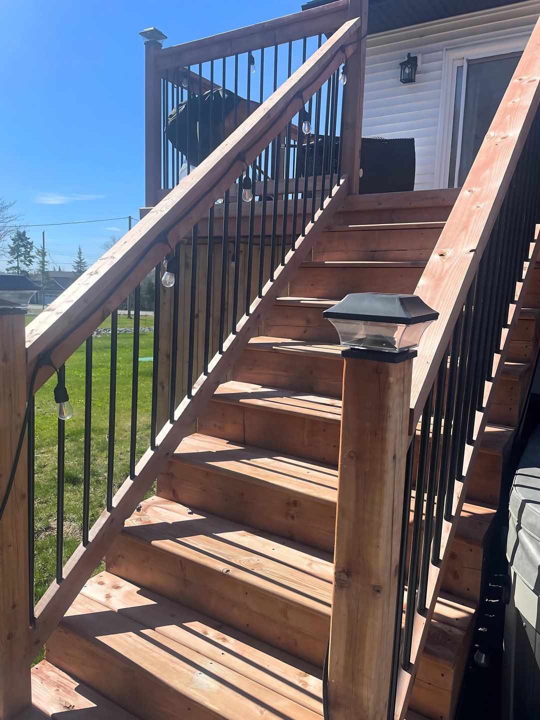 A set of custom made wooden stairs leading up to a deck with black railings. 